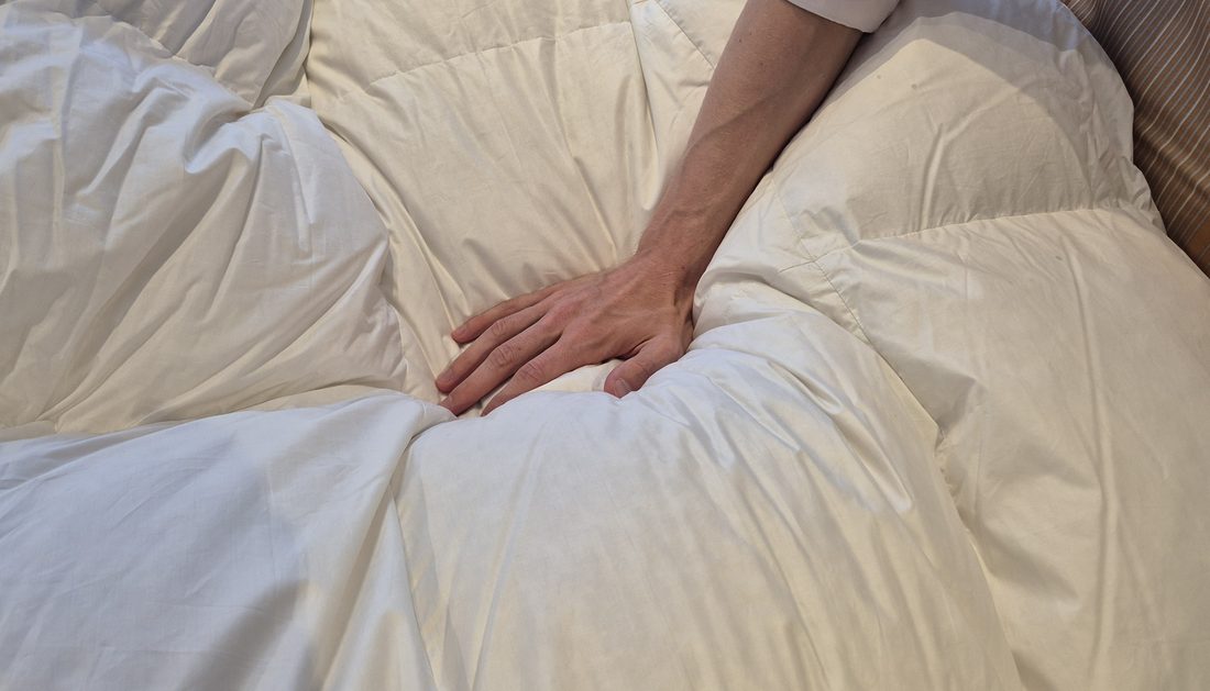 Eine Hand drückt in eine Daunendecke, der Stoff legt sich in weiche Falten.